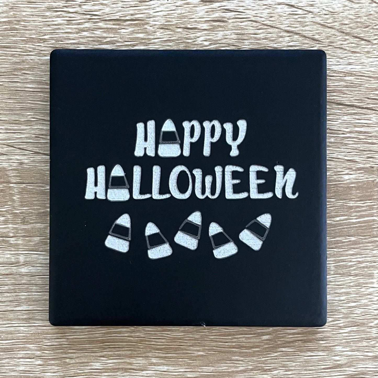 Black square coaster with Happy Halloween text and candy corn
