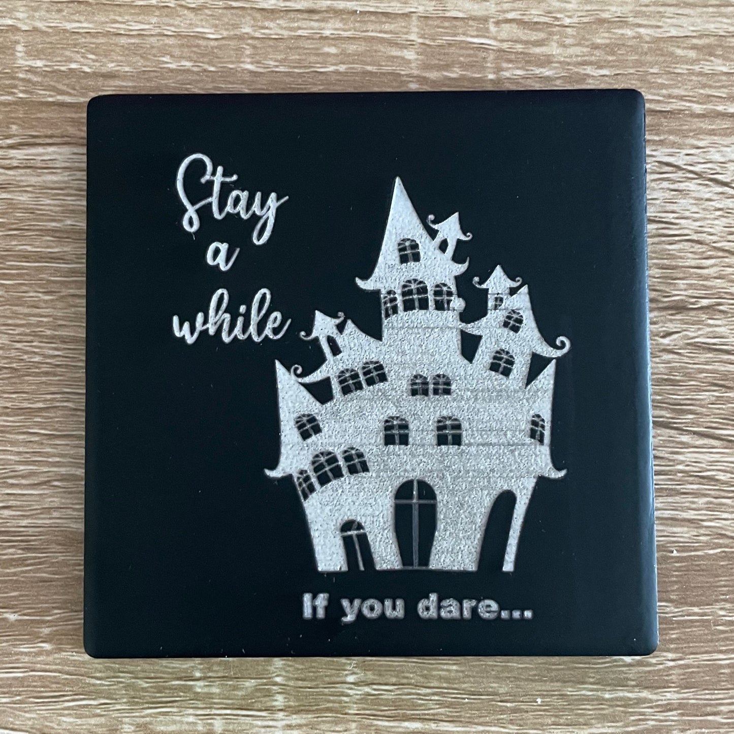 Black square haunted house coaster with message "stay a while...if you dare"