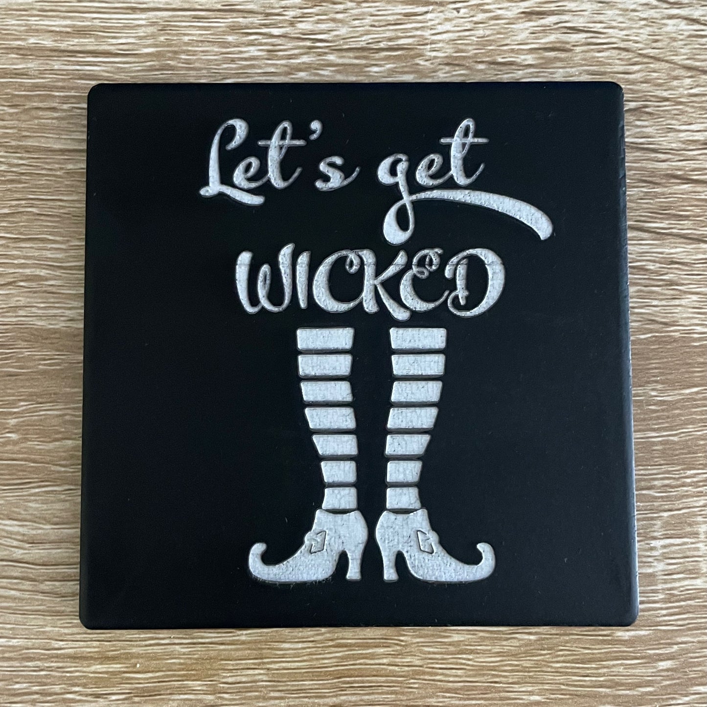 Black square Halloween coaster with "let's get wicked" text and striped witch's socks and heels