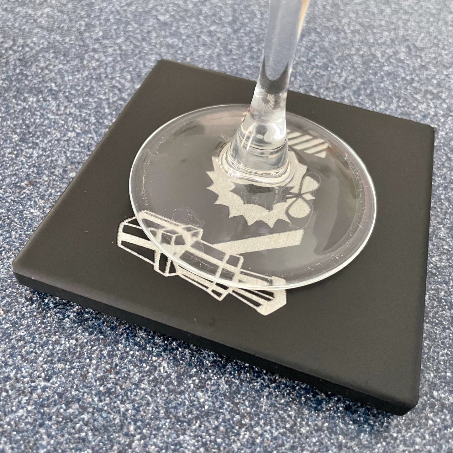Black square ceramic engraved coaster with stemmed wine glass sitting on top