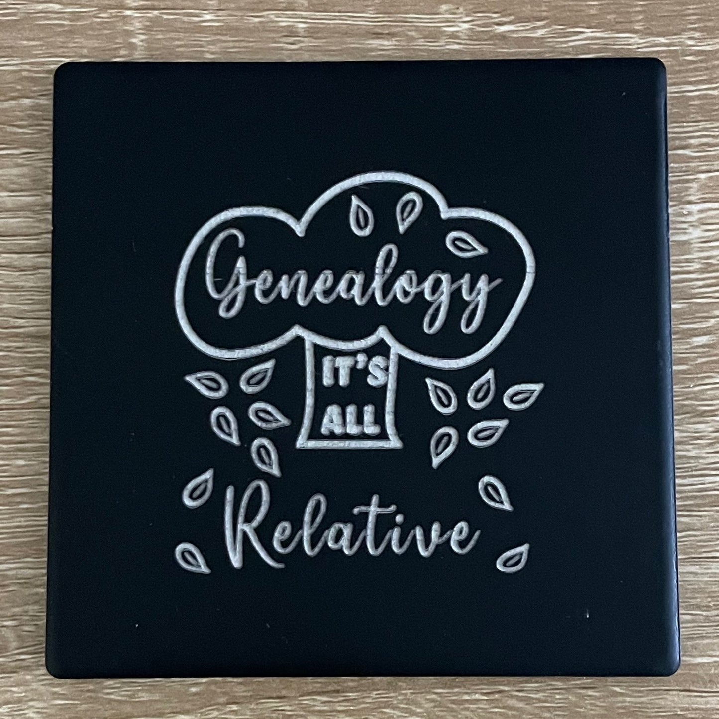 Black ceramic square coaster engraved with phrase "Genealogy It's All Relative" and tree with falling leaves