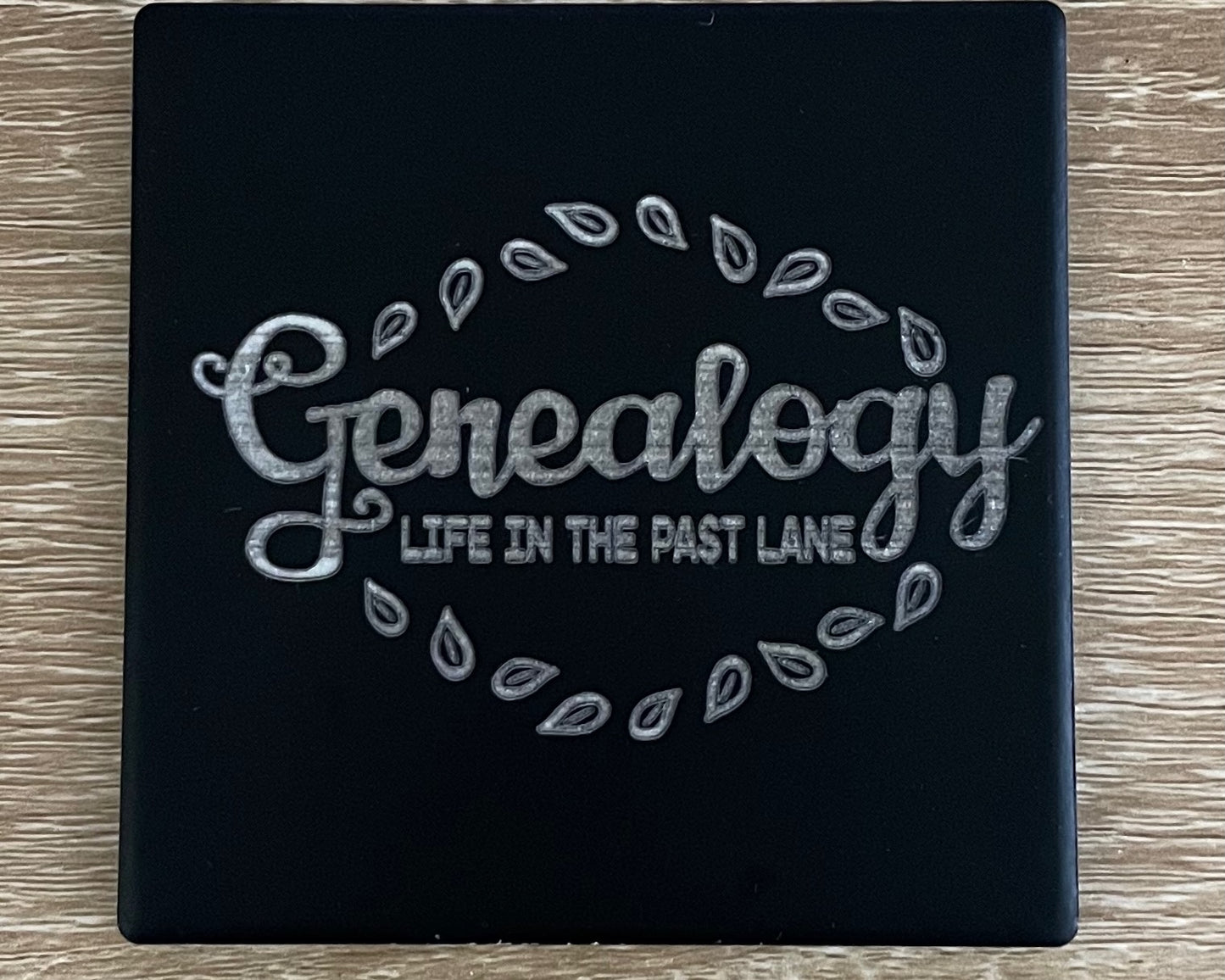 Black ceramic square coaster engraved with "genealogy life in the past lane"