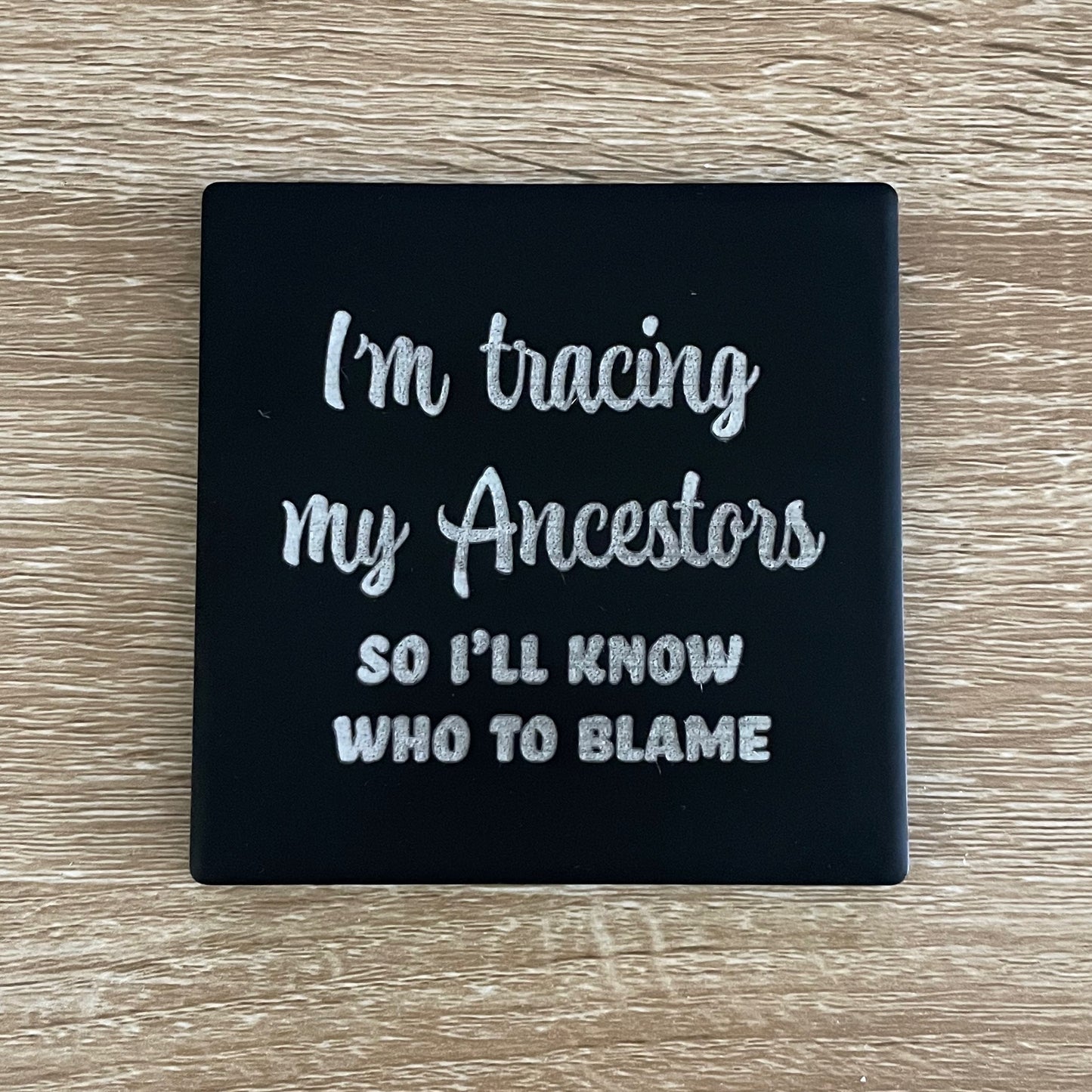 Black ceramic square coaster engraved with genealogy phrase "I'm tracing my ancestors so I'll know who to blame"
