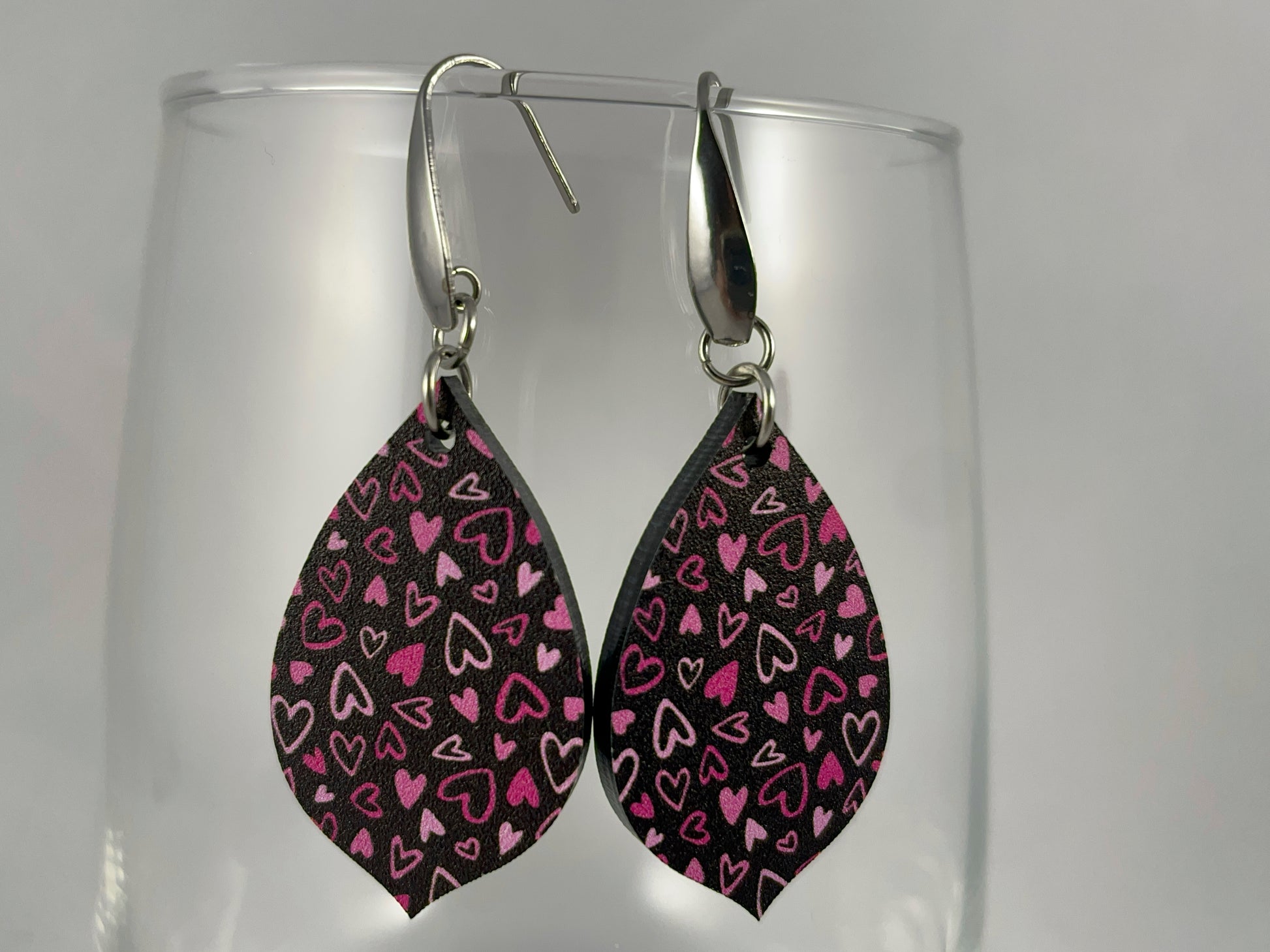 Close-up view of Pink on Black Micro-Print Hearts teardrop shaped acrylic earrings on stainless steel ear wires 