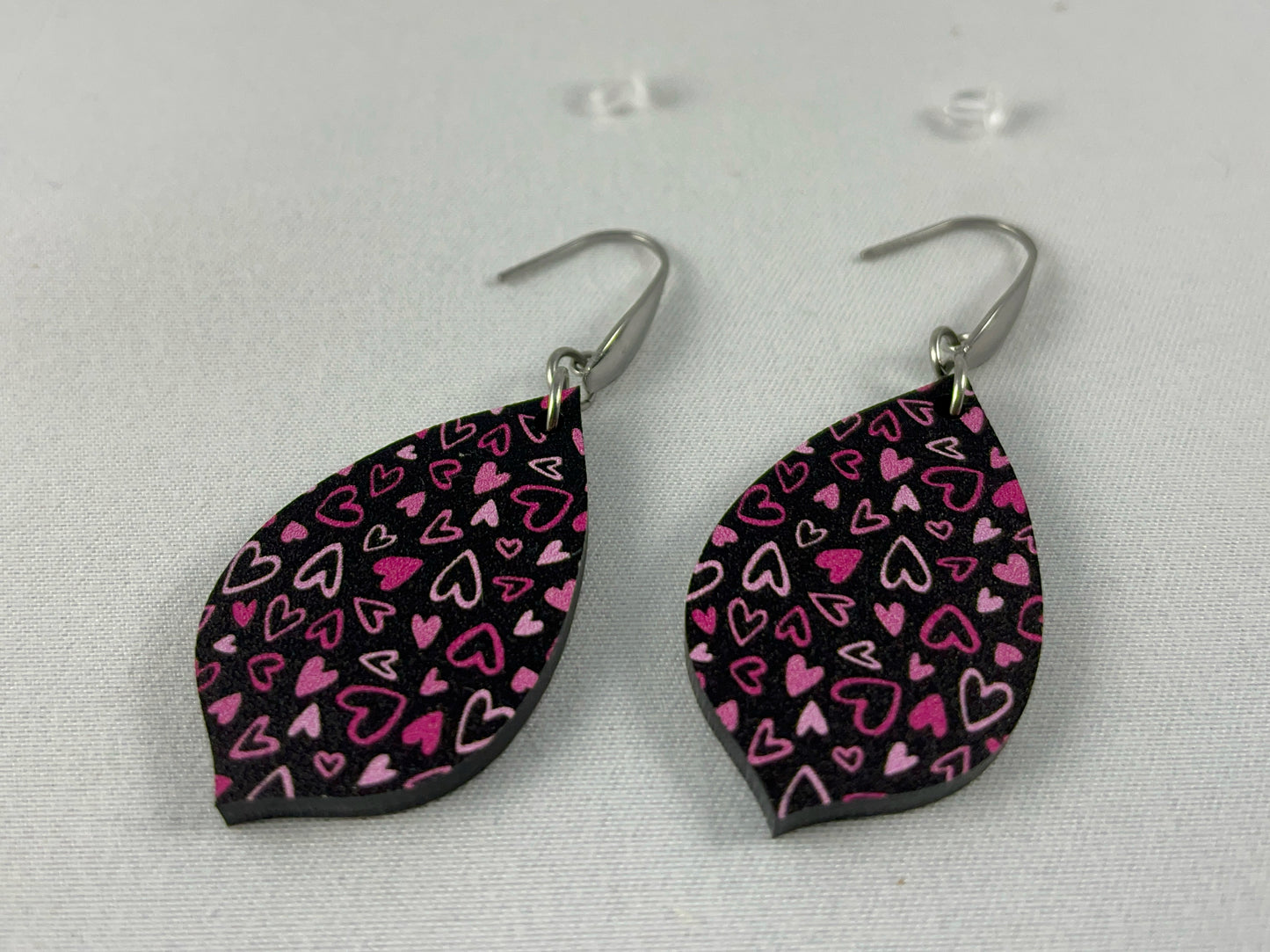 Detail view of Pink on Black Micro-Print Hearts teardrop shaped acrylic earrings on stainless steel ear wires  