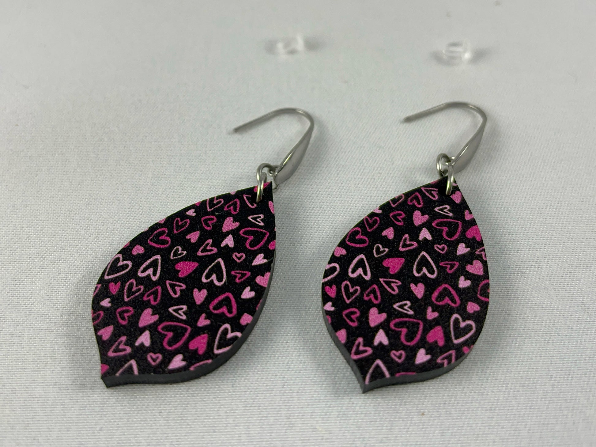 Detail view of Pink on Black Micro-Print Hearts teardrop shaped acrylic earrings on stainless steel ear wires  