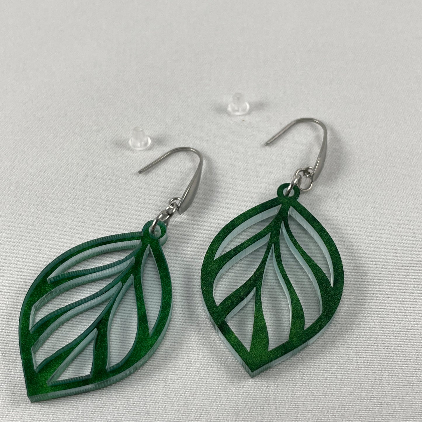 Detail view of acrylic laser cut leaf pattern dangle earrings on stainless steel ear wires with teardrop feature and included silicone earring backs