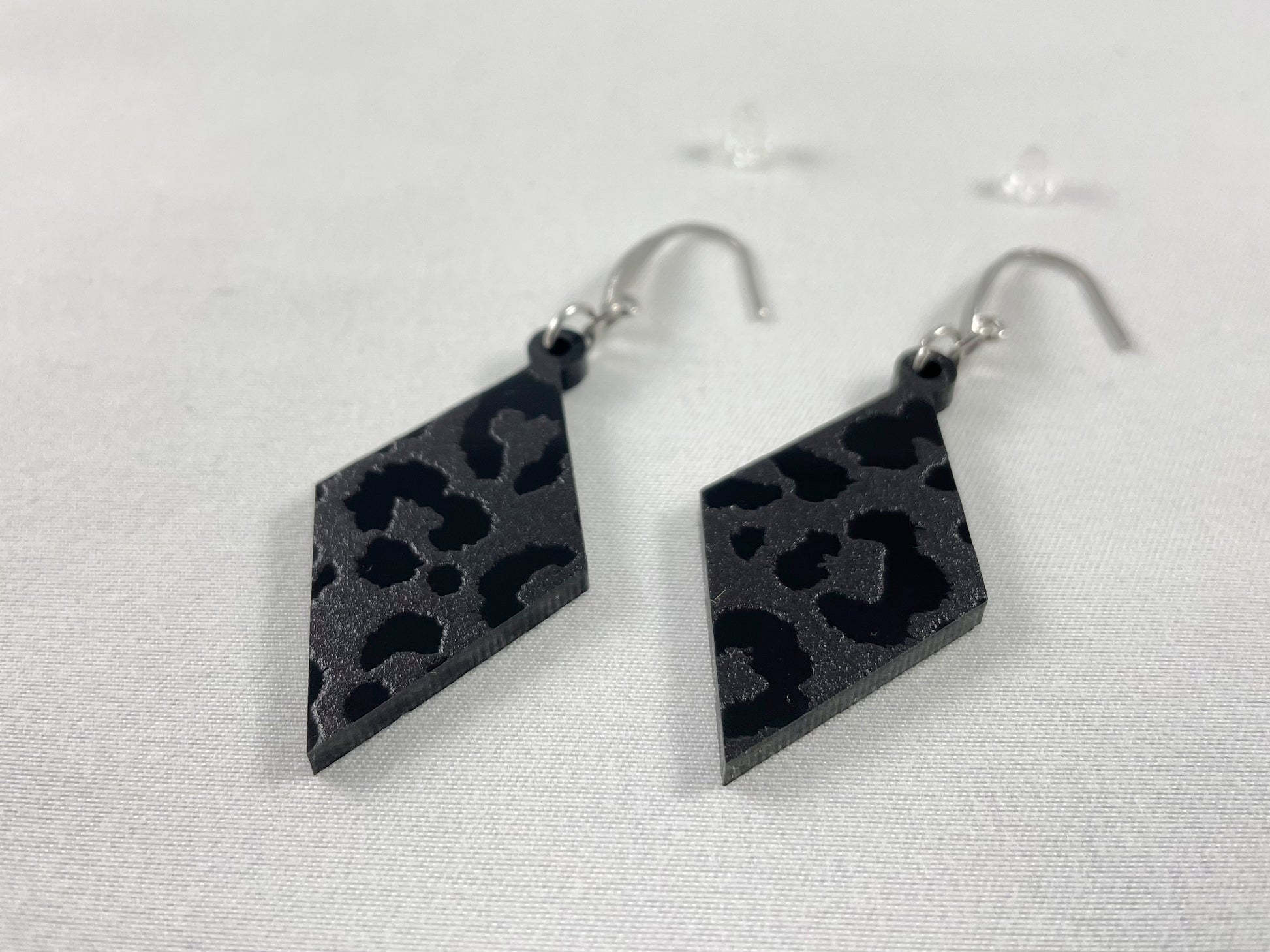 Detail view of Diamond-shaped leopard print black on black ac relic earrings on stainless steel ear wires with teardrop accent