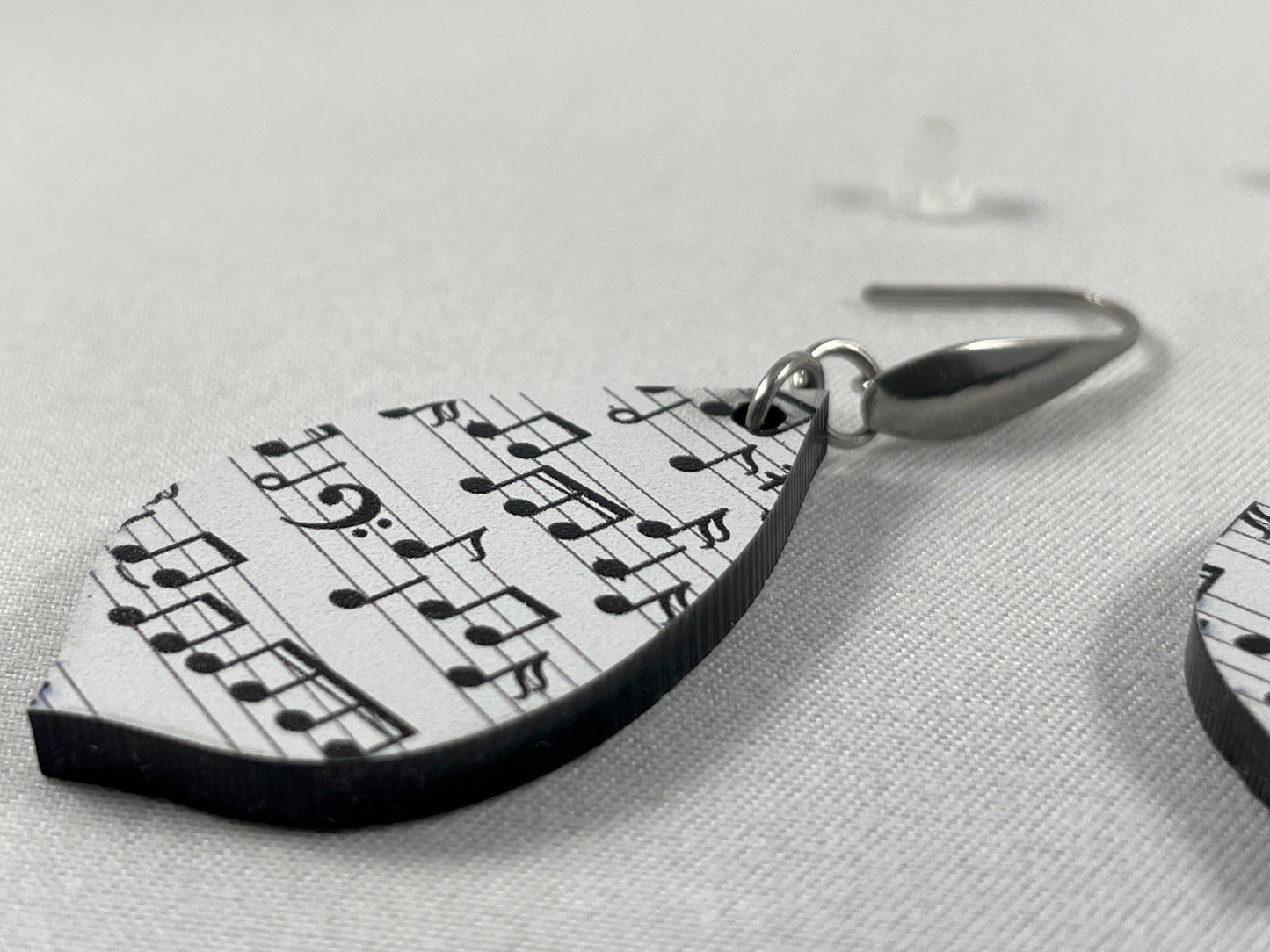 Close-up view of acrylic earrings with black music notes on white background and stainless steel ear wires with teardrop accent