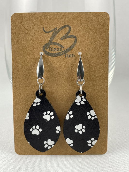 Black acrylic teardrop shaped dangle earrings with white paw prints and stainless steel ear wires with teardrop accent