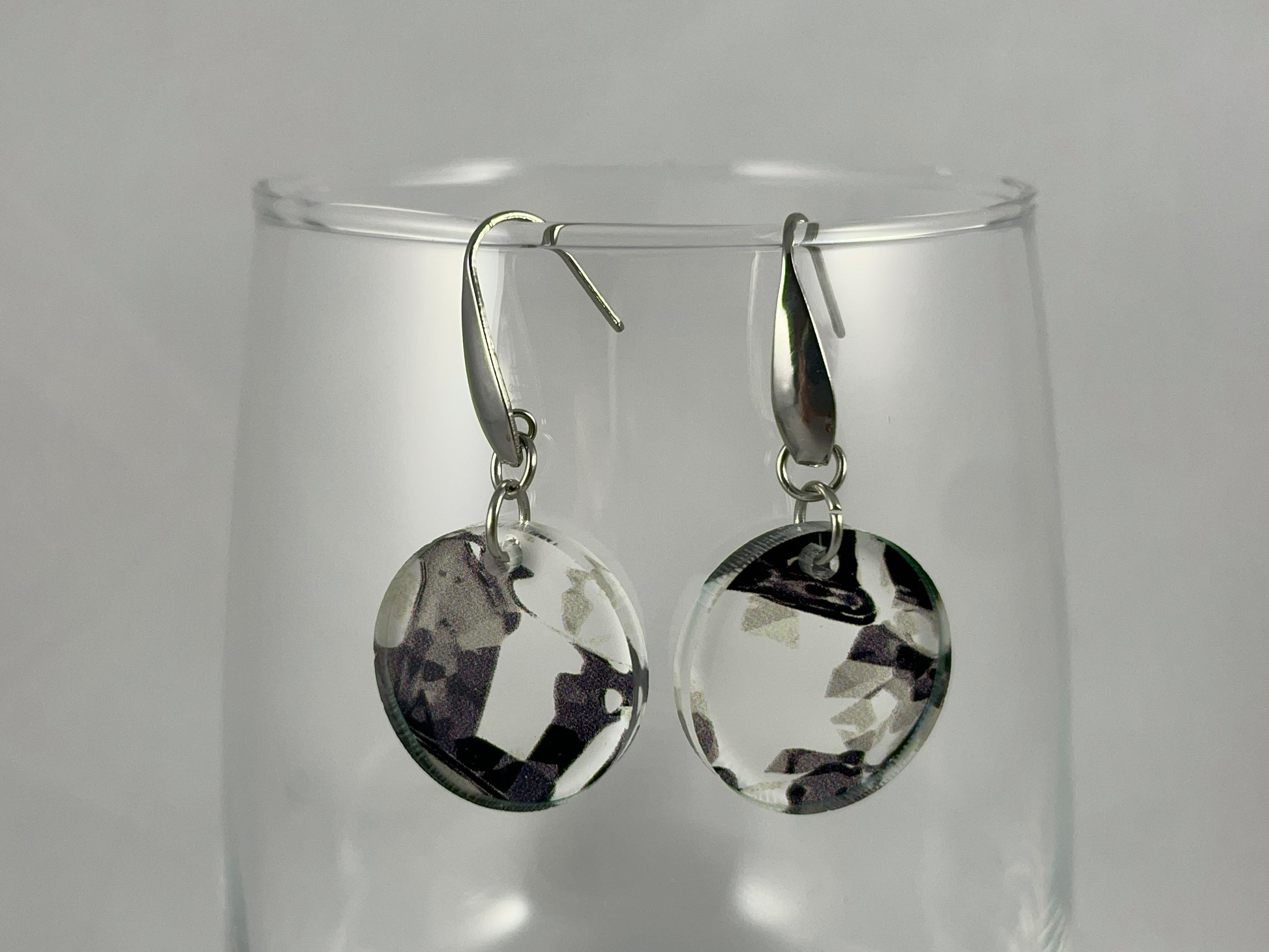 Close-up view of small round abstract black and white acrylic dangle earrings on stainless steel ear wires with teardrop accent