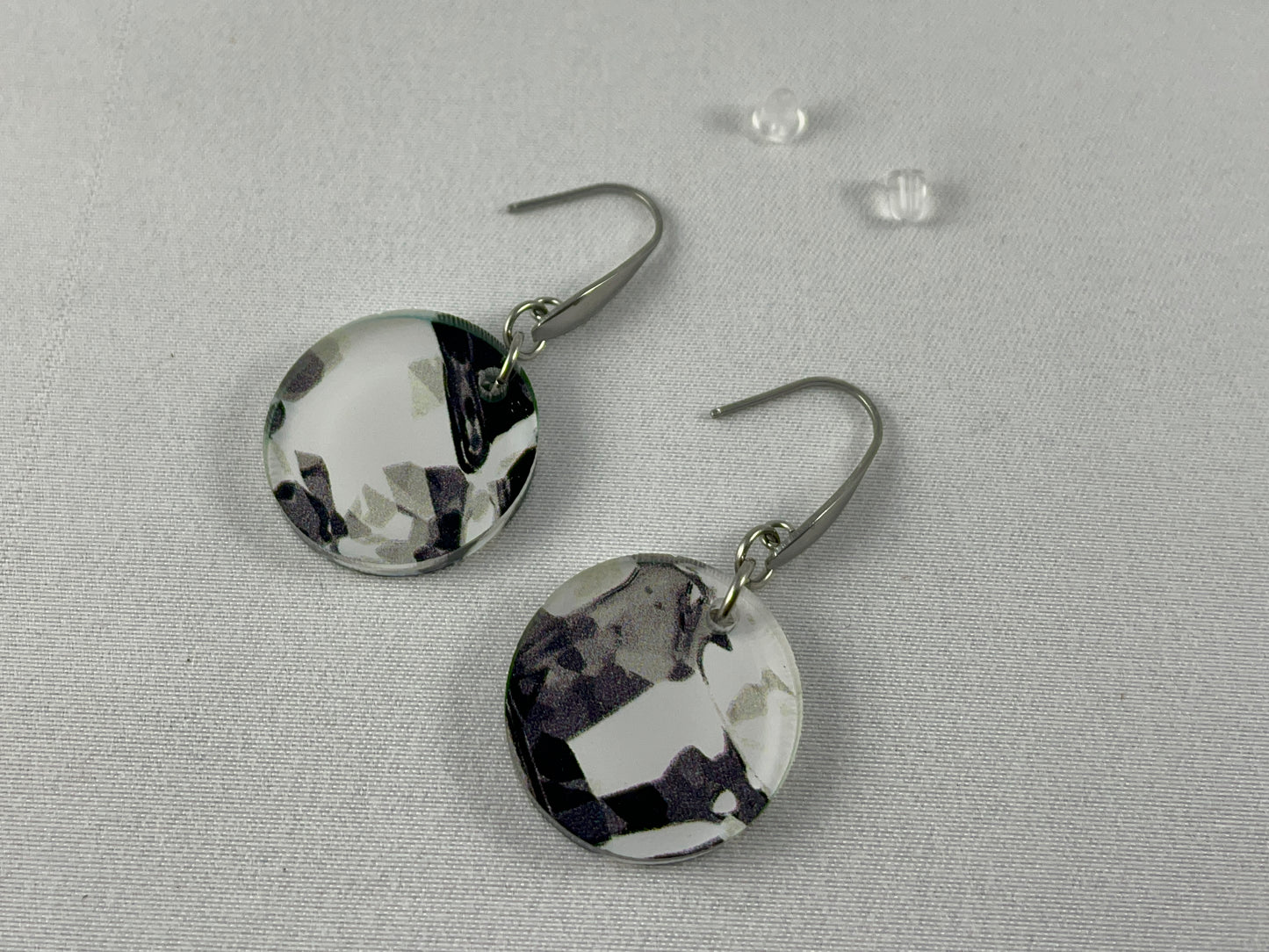 Detail view of small round abstract black and white acrylic dangle earrings on stainless steel ear wires with teardrop accent