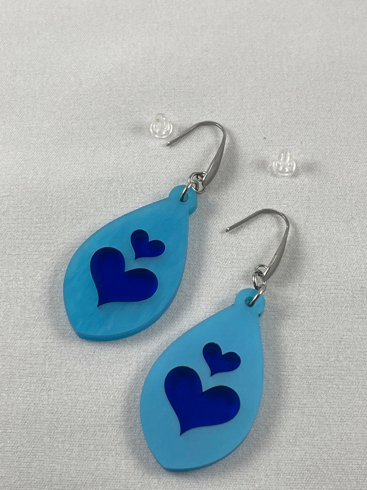 Detail view of light blue acrylic teardrop earrings with lapis blue inlay hearts on stainless steel ear wires with teardrop accent and included silicone earring backs