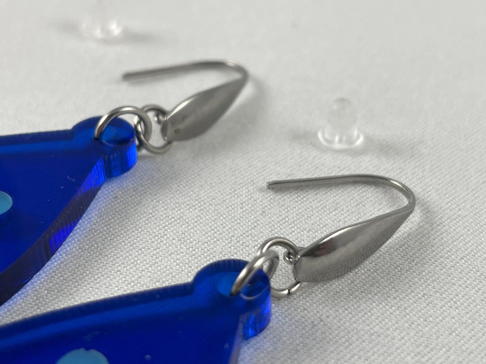 Close-up of lapis blue acrylic teardrop earrings with light blue inlay hearts on stainless steel ear wires with teardrop accent and included silicone earring backs