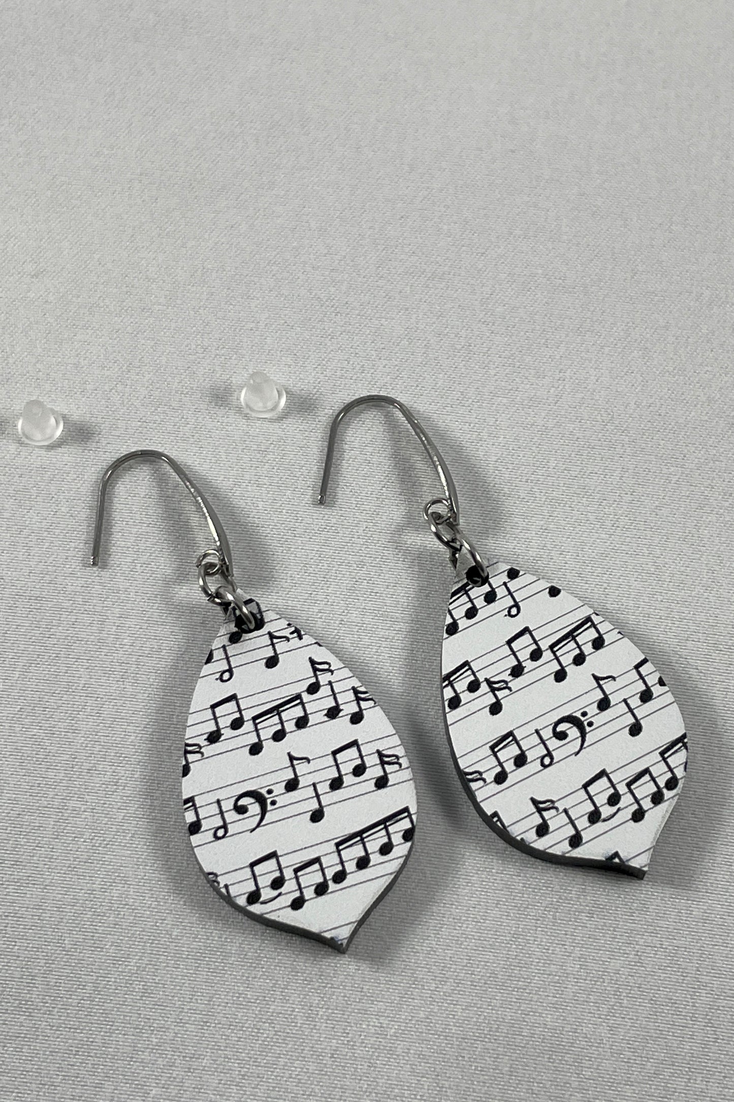 Detail view of Acrylic earrings with black music notes on white background and stainless steel ear wires with teardrop accent and included silicone earring backs