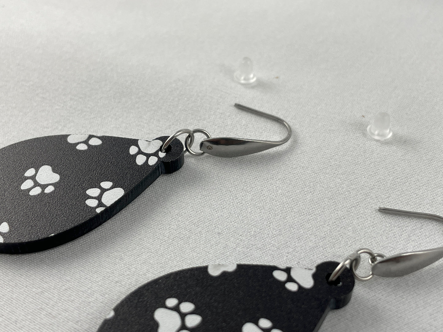 Close-up view of Black acrylic teardrop shaped dangle earrings with white paw prints and stainless steel ear wires with teardrop accent