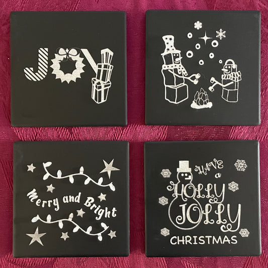 Set of four square black ceramic coasters engraved with Christmas themed images and phrases including JOY, Merry and Bright, Holly Jolly Christmas, Snowmen, Candy Cane, Wreath, Gift Packages, C9 lights